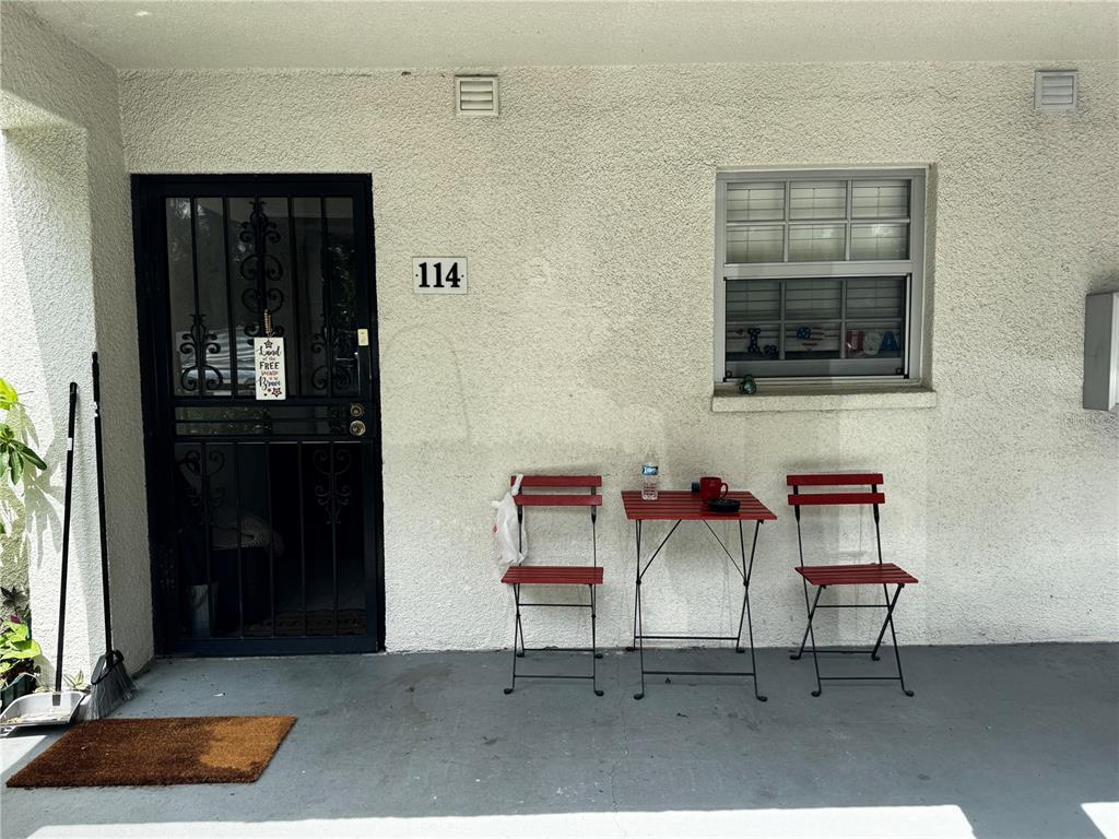 A patio area features a black security door, a window, and a small red bistro set — 706 OAKGROVE DRIVE UNIT 114, BRANDON, FL