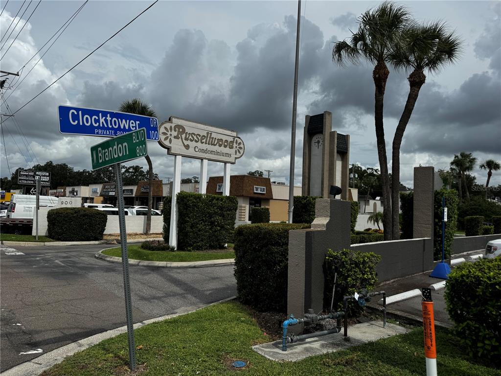 A street sign for Clocktower Drive and Brandon Boulevard stands before the Russellwood Condominiums entrance — 706 OAKGROVE DRIVE UNIT 114, BRANDON, FL
