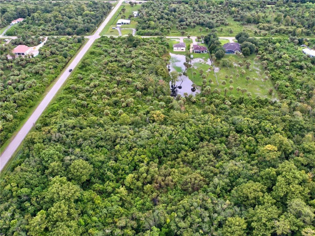 An aerial view shows a wooded lot with a pond near several residential houses — SHADY HOLLOW BOULEVARD E, NAPLES, FL