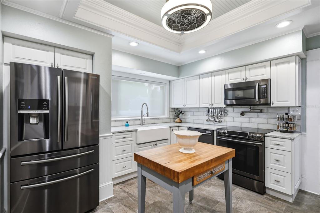A kitchen with white cabinets, stainless steel appliances, a butcher block island, and tile flooring — 47 DAVIS AVENUE, UMATILLA, FL