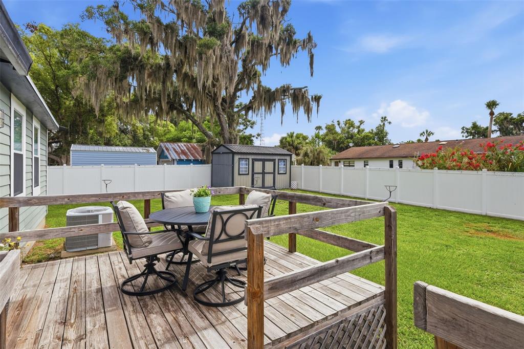 A wooden deck with patio furniture overlooks a grassy backyard enclosed by a white fence — 47 DAVIS AVENUE, UMATILLA, FL