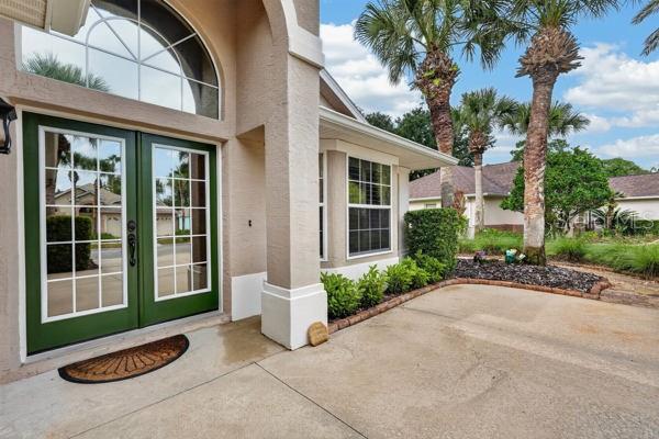 A beige house exterior features a green double front door and a concrete driveway — 54 SHINNECOCK DRIVE, PALM COAST, FL