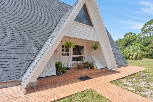 The exterior of an A-frame house features a brick walkway leading to a covered porch — 2121 DRESSAGE COVE, CHULUOTA, FL