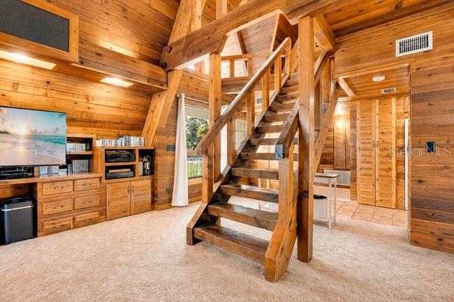 A rustic wood-paneled room features a staircase, a television, and built-in storage cabinets — 2121 DRESSAGE COVE, CHULUOTA, FL