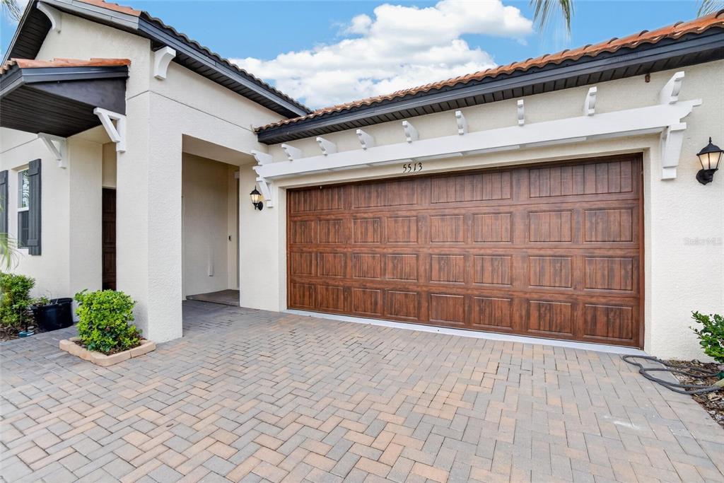 A paved driveway leads to a two-car garage with a wood-look door and white pergola — 5513 LITTLE PATH DRIVE, WIMAUMA, FL