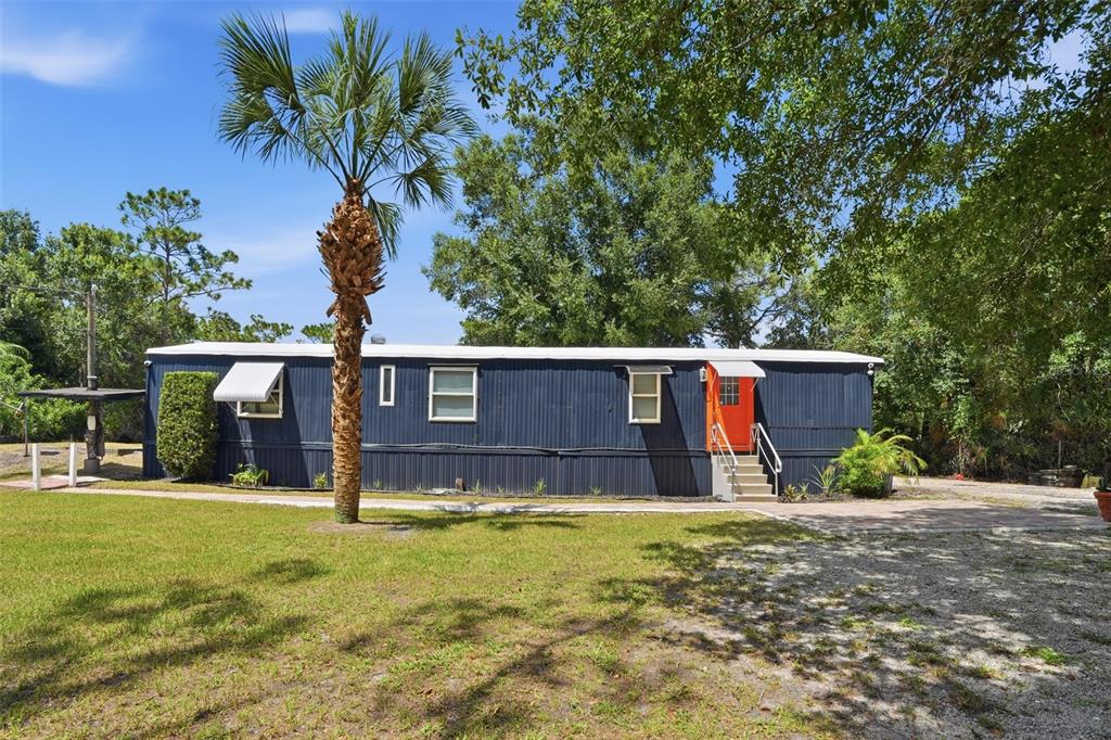 A dark blue mobile home with an orange door sits on a grassy lot — 9295 LUNA DRIVE, ST CLOUD, FL