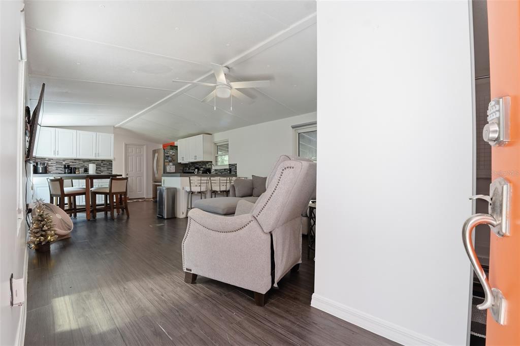 An open-concept living room and kitchen feature dark wood flooring and a light gray recliner — 9295 LUNA DRIVE, ST CLOUD, FL