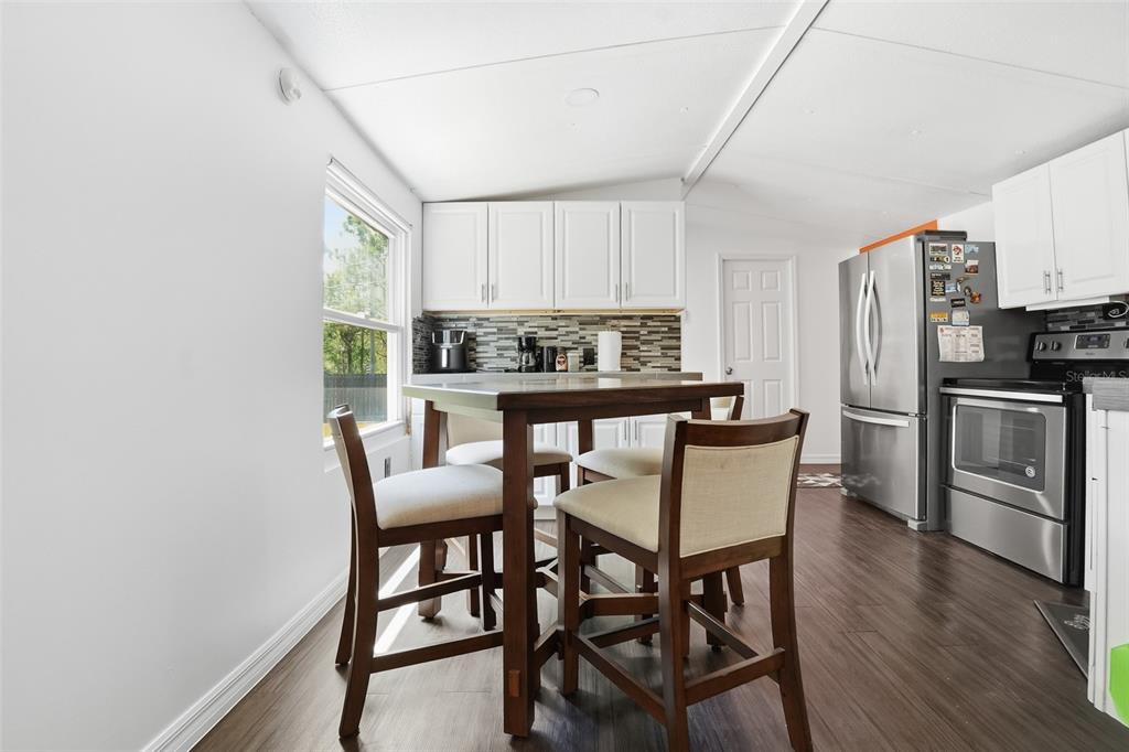 A kitchen features white cabinets, stainless steel appliances, a dining table, and wood-look flooring — 9295 LUNA DRIVE, ST CLOUD, FL
