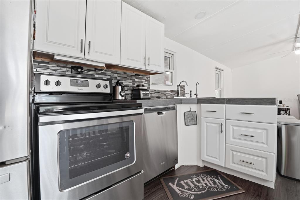 A kitchen features stainless steel appliances, white cabinets, and a gray tiled backsplash — 9295 LUNA DRIVE, ST CLOUD, FL
