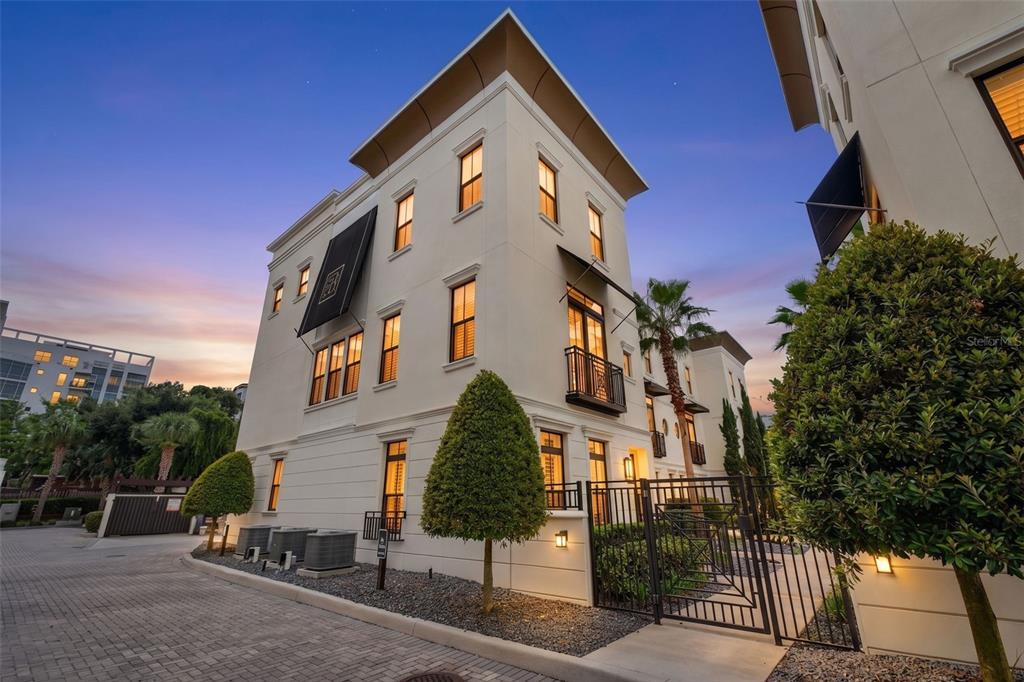 A multi-story white stucco townhouse with black awnings and a gated entrance at dusk — 636 MARIPOSA STREET, ORLANDO, FL