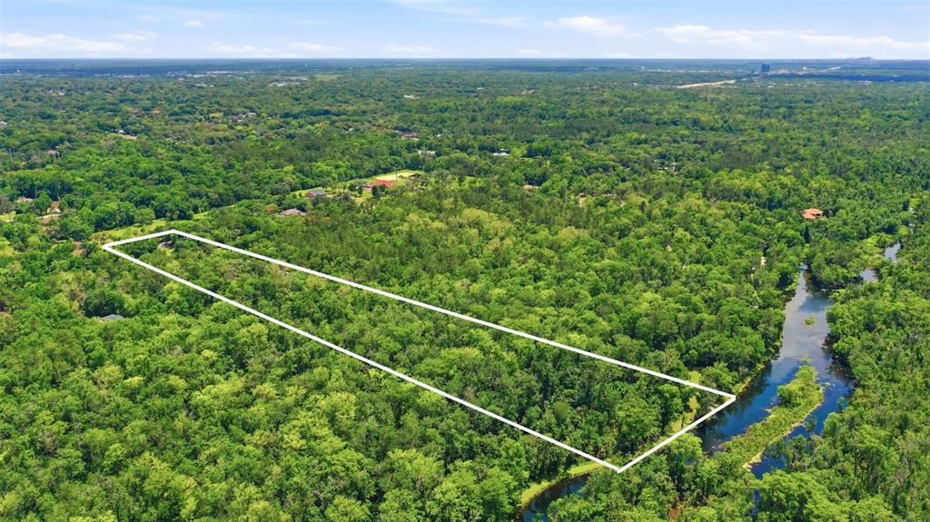 An aerial view shows a rectangular plot of land outlined in white amidst dense forest — DELK ROAD, LONGWOOD, FL