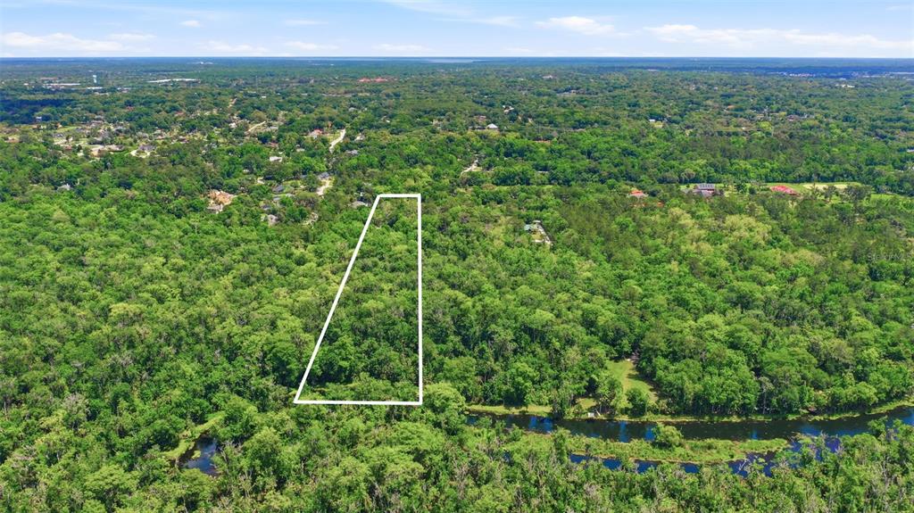 An aerial view shows a wooded plot of land outlined in white near a river — DELK ROAD, LONGWOOD, FL