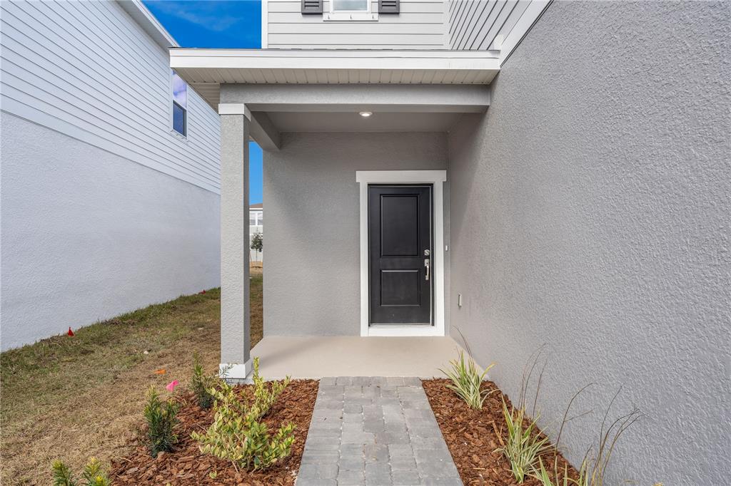 A gray house exterior features a covered entryway with a black door and stone walkway — 876 CASTLEFORD AVENUE NE, PALM BAY, FL