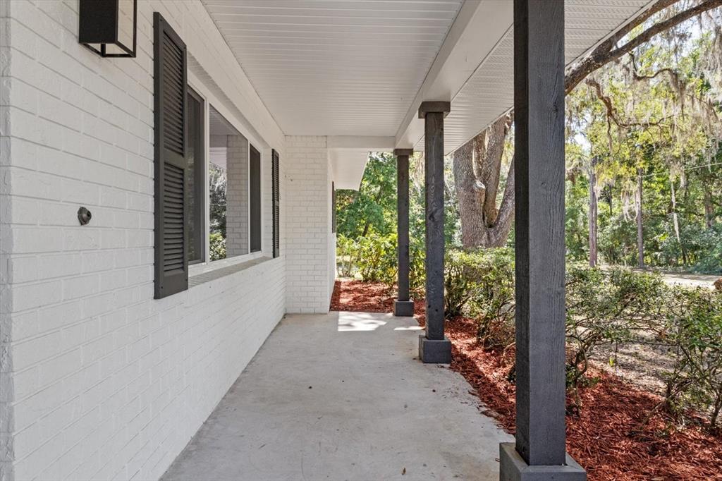 A covered concrete porch features white brick walls, dark shutters, and dark wooden support posts — 1255 S ESTATE POINT, INVERNESS, FL