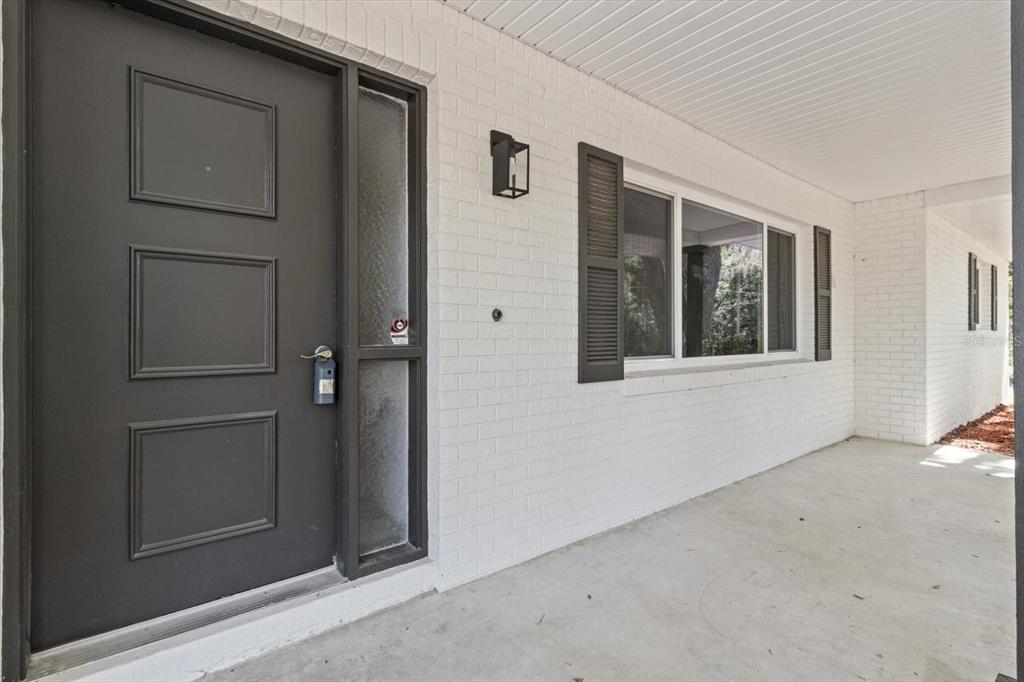 A white brick exterior wall features a dark gray front door and a large window — 1255 S ESTATE POINT, INVERNESS, FL