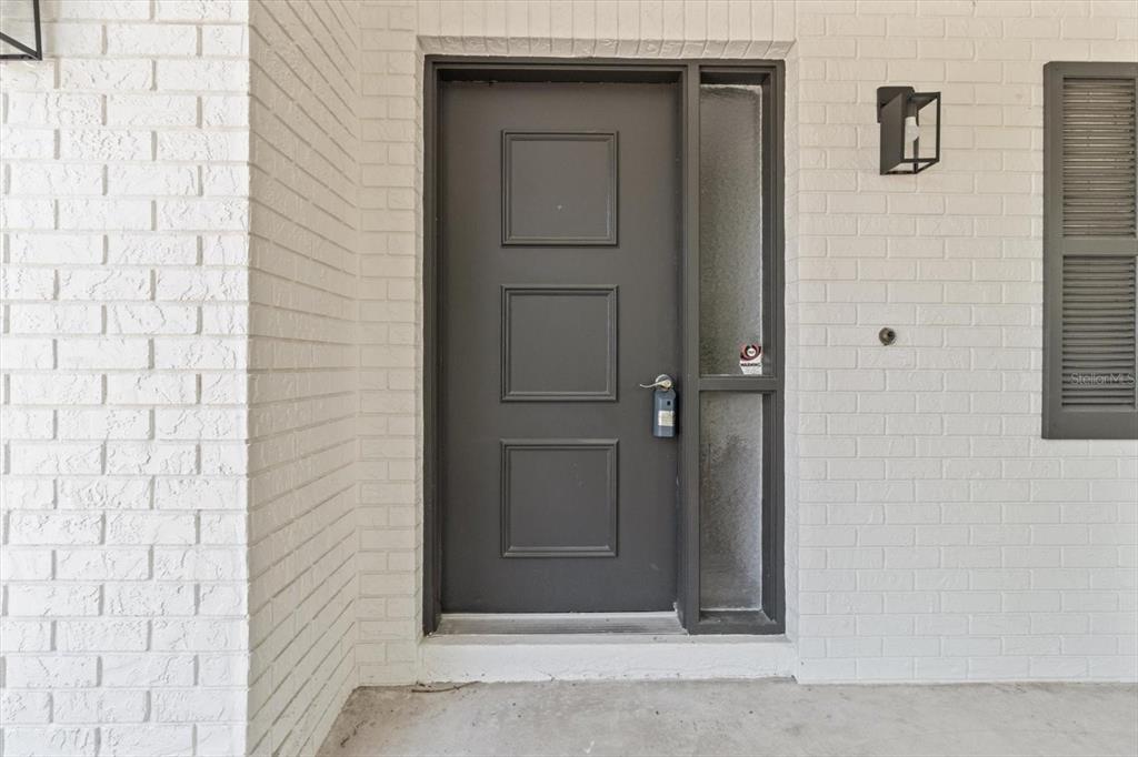 A dark gray front door with three panels sits in a white painted brick wall — 1255 S ESTATE POINT, INVERNESS, FL