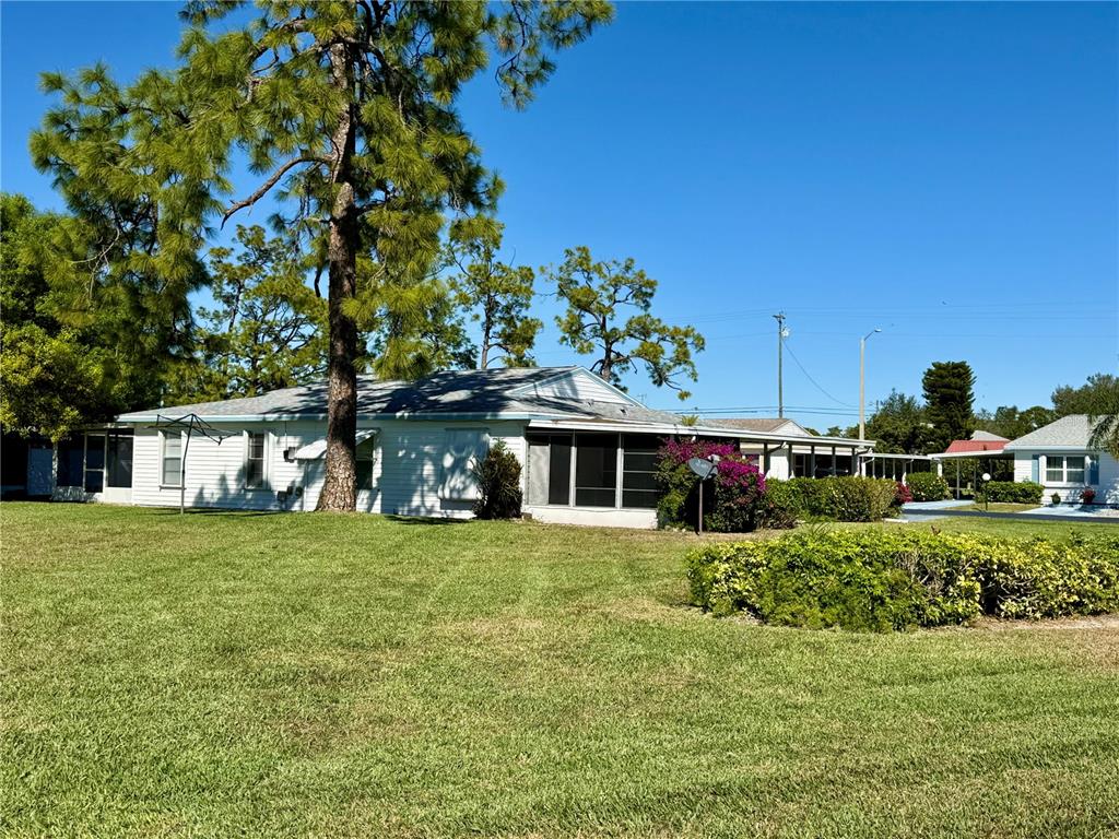 A white single-story house with a screened-in porch sits on a large grassy lawn — 7 DESERT CANDLE CIRCLE, LEHIGH ACRES, FL