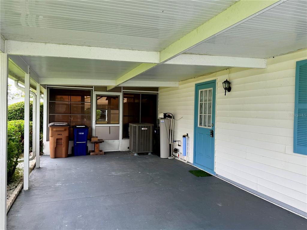 A covered carport features a concrete floor, a blue door, and outdoor utility equipment — 7 DESERT CANDLE CIRCLE, LEHIGH ACRES, FL