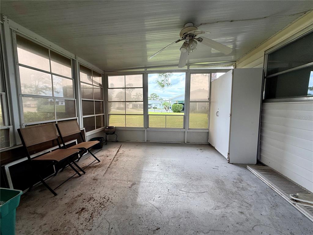 A screened-in porch with a concrete floor, ceiling fan, and large windows overlooking a yard — 7 DESERT CANDLE CIRCLE, LEHIGH ACRES, FL