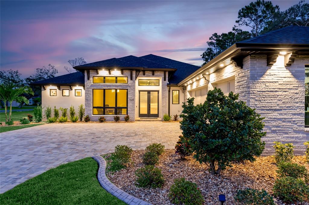 A modern single-story house with a stone facade, dark roof, and a paved driveway at dusk — 1625 TURNBULL CROSSINGS DRIVE, NEW SMYRNA BEACH, FL
