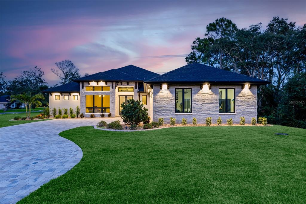 A single-story house with a stone facade, dark roof, and a paved driveway at dusk — 1625 TURNBULL CROSSINGS DRIVE, NEW SMYRNA BEACH, FL