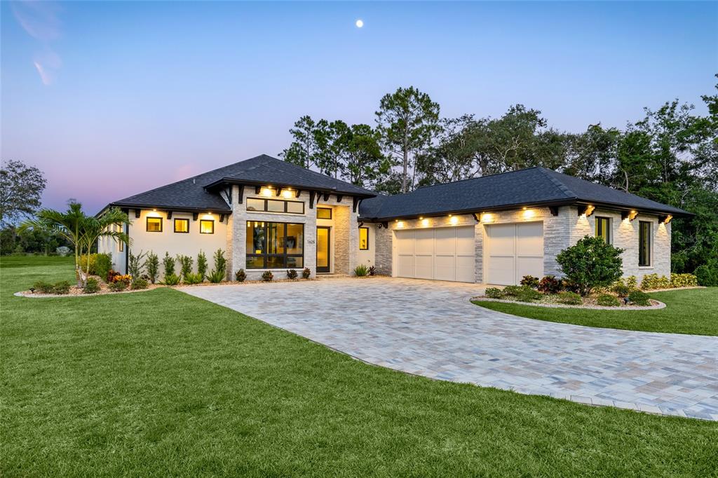 A modern single-story house with a stone facade, dark roof, and a paved driveway at dusk — 1625 TURNBULL CROSSINGS DRIVE, NEW SMYRNA BEACH, FL