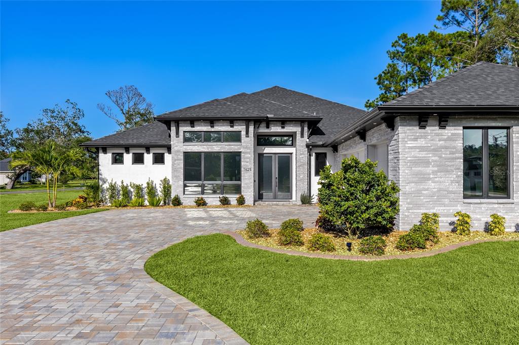 A modern single-story house with a gray brick exterior, dark trim, and a paved driveway — 1625 TURNBULL CROSSINGS DRIVE, NEW SMYRNA BEACH, FL