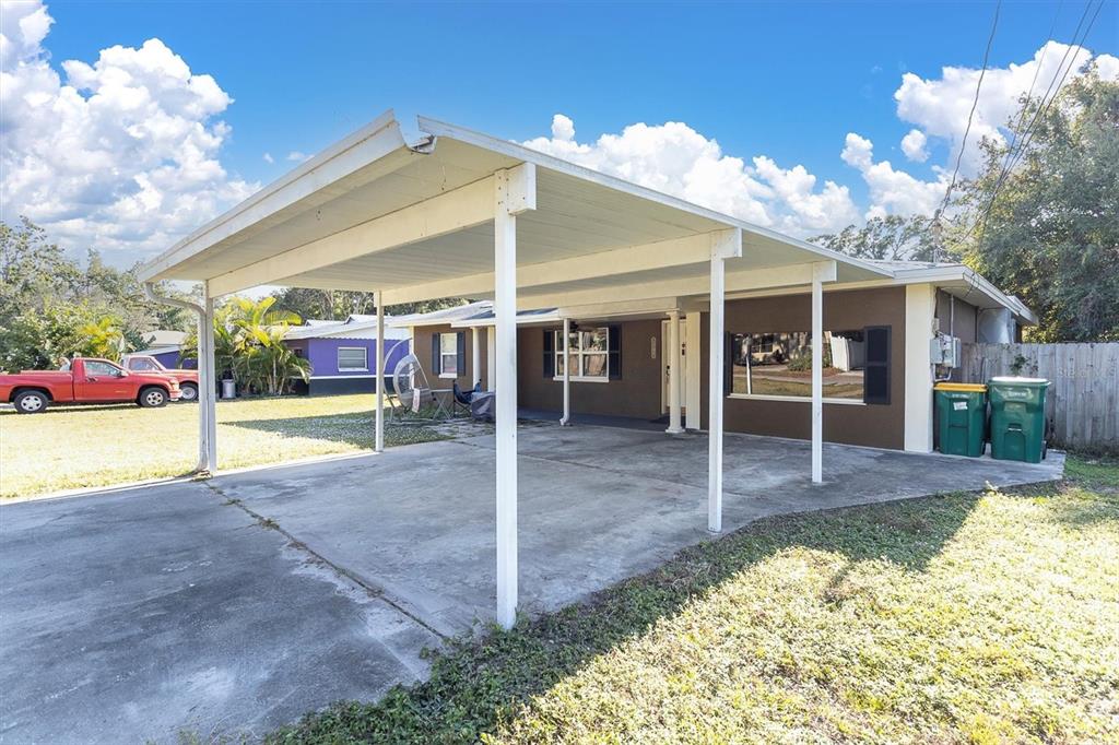 A brown single-story house features a large concrete driveway covered by a white metal carport — 1797 RAINBOW BOULEVARD, CLEARWATER, FL