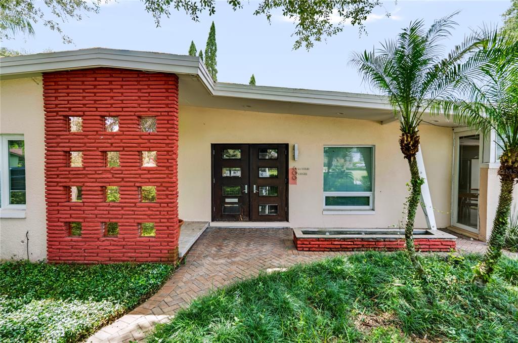 The exterior of a mid-century modern home features a red brick accent wall with glass blocks — 600 MAYFAIR CIRCLE, ORLANDO, FL
