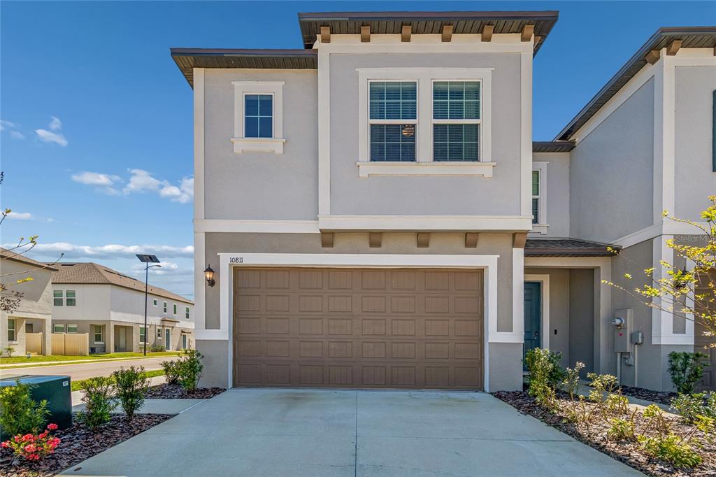 A two-story townhouse exterior with a brown garage door, gray stucco walls, and a sidewalk — 10811 FOWLERS BLUFF COURT, TAMPA, FL