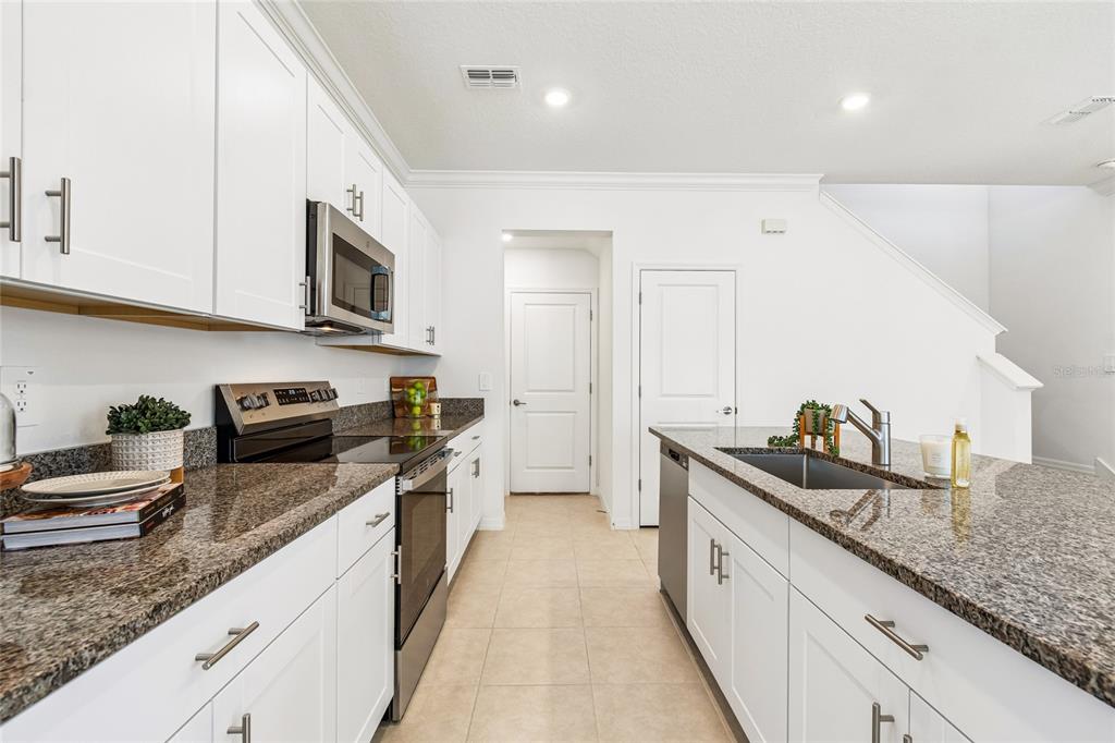 A modern kitchen features white cabinets, granite countertops, an island, and light-colored tile flooring — 10811 FOWLERS BLUFF COURT, TAMPA, FL