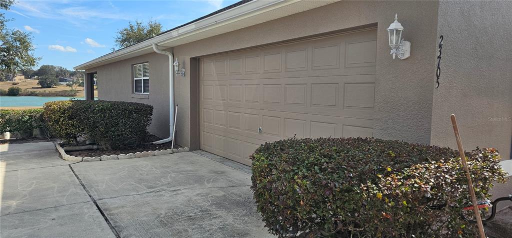 A tan stucco house features a two-car garage, a concrete driveway, and a landscaped bush — 23705 MILFORD DRIVE, EUSTIS, FL