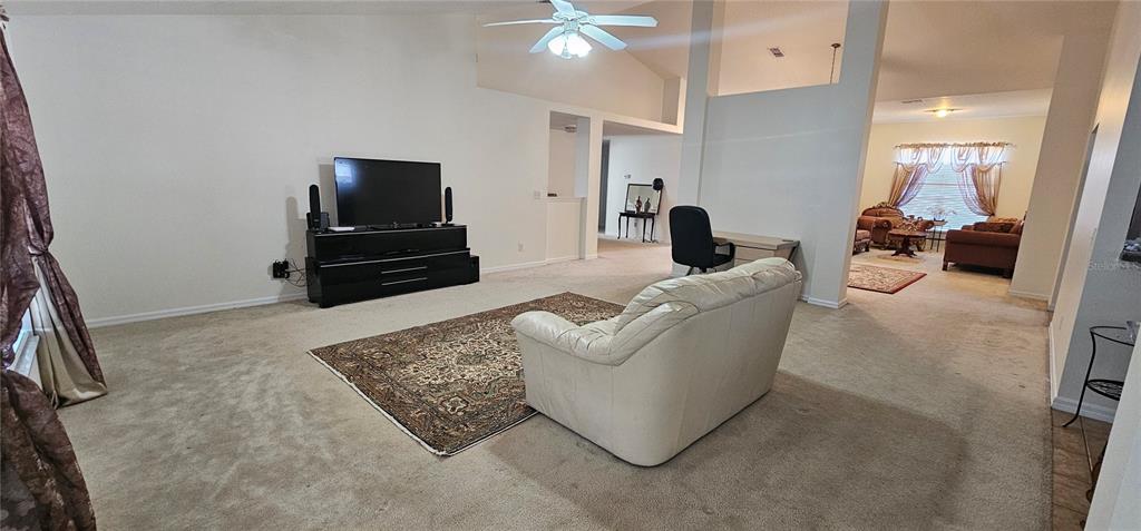 A living room features beige carpet, a white sofa, and a television on a stand — 23705 MILFORD DRIVE, EUSTIS, FL