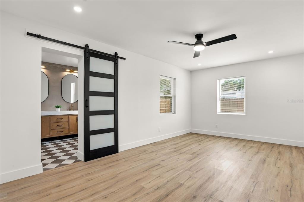 A bedroom with light wood flooring, a ceiling fan, and a black sliding barn door — 900 CARVER STREET, WINTER PARK, FL