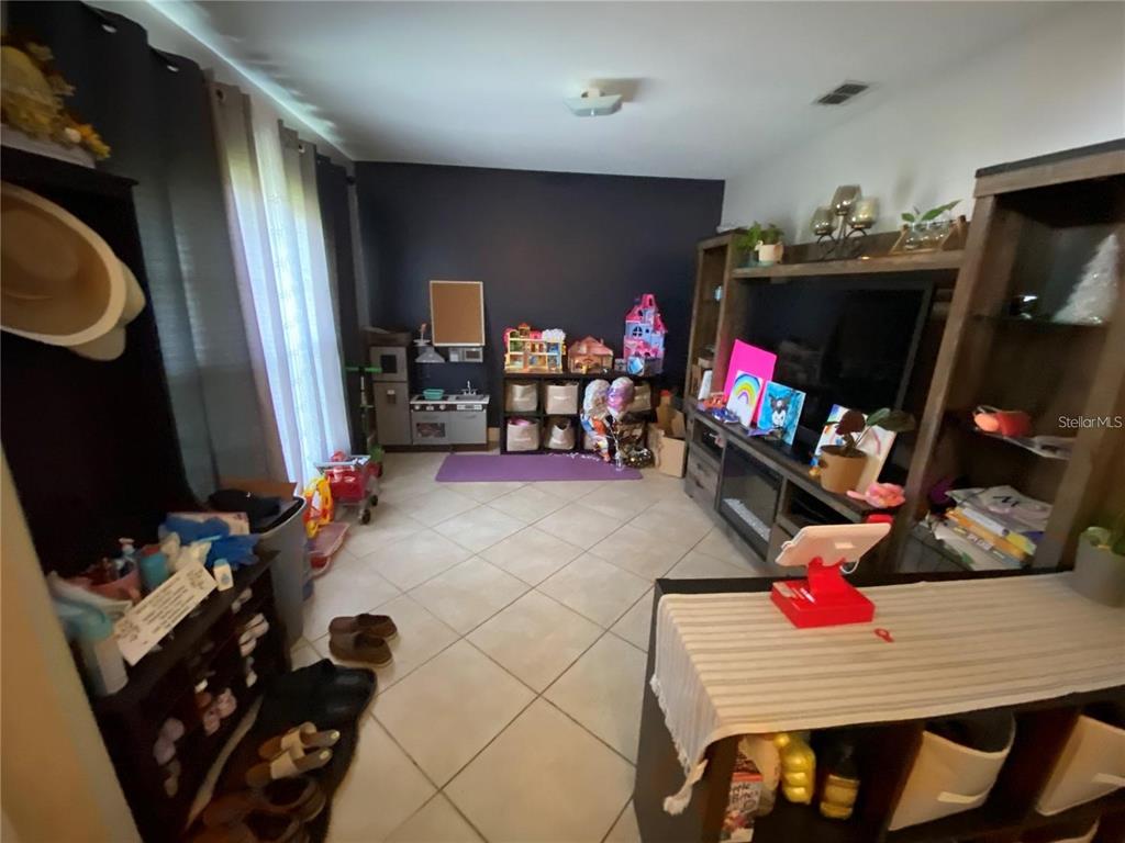 A living room with tile flooring, a dark accent wall, and various children's toys — 1953 THE OAKS BOULEVARD, KISSIMMEE, FL
