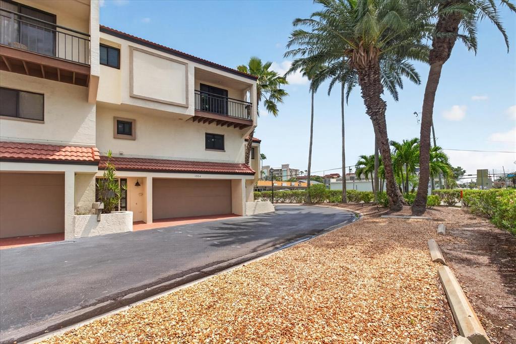 A multi-story townhouse exterior features two garage bays, balconies, and palm trees nearby — 240 WINDWARD PASSAGE UNIT 1004, CLEARWATER BEACH, FL