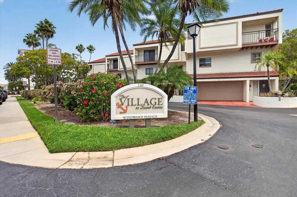 The exterior of a multi-story apartment complex features a prominent community sign and palm trees — 240 WINDWARD PASSAGE UNIT 1004, CLEARWATER BEACH, FL