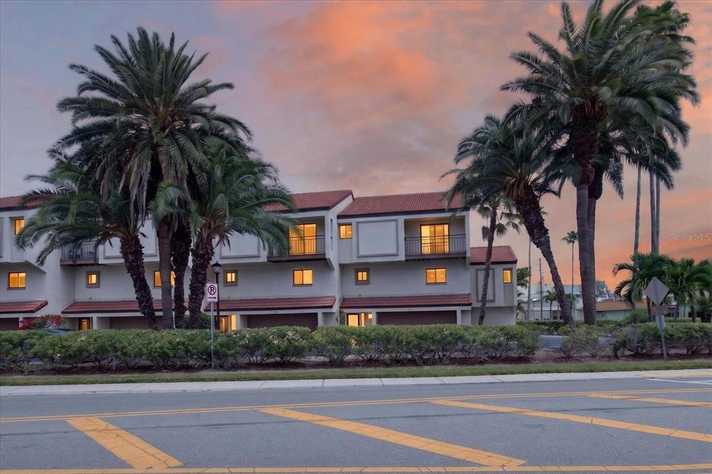 A multi-story townhouse complex with palm trees and a sunset sky in the background — 240 WINDWARD PASSAGE UNIT 1004, CLEARWATER BEACH, FL