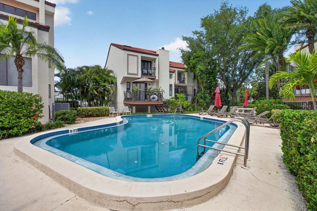A swimming pool sits in front of a multi-story residential building with palm trees — 240 WINDWARD PASSAGE UNIT 1004, CLEARWATER BEACH, FL
