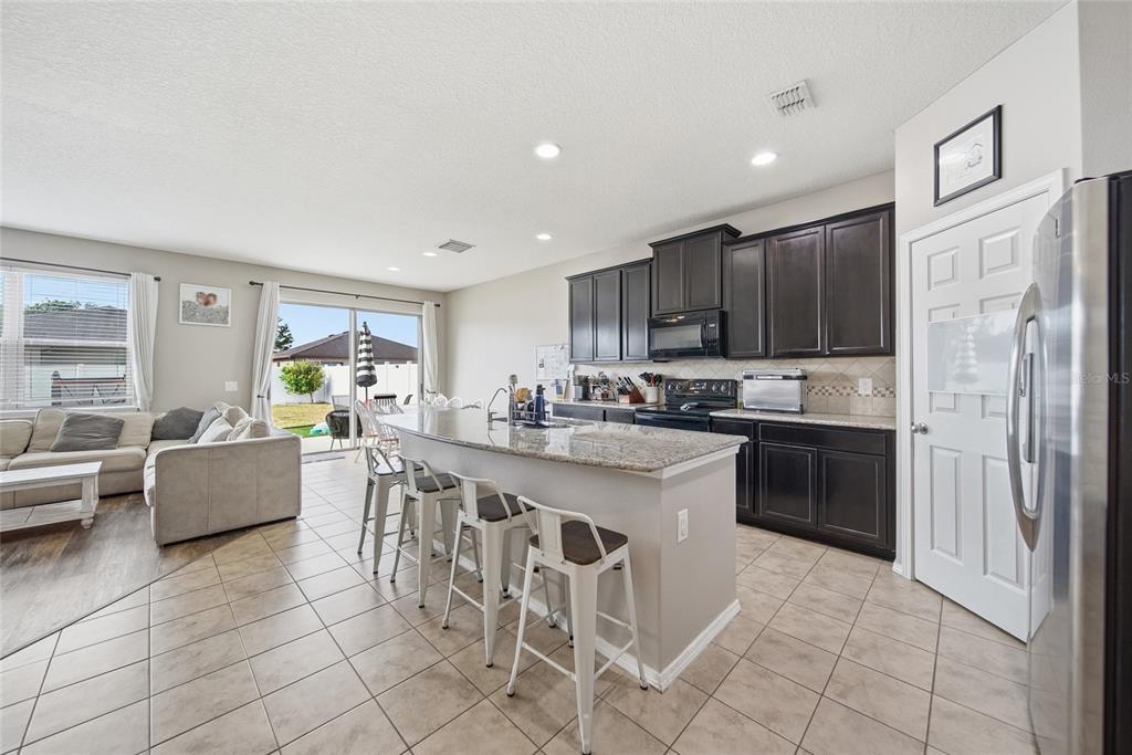 An open-concept living room features wood-look flooring, a sectional sofa, and an adjacent kitchen — 15476 STONE HOUSE DRIVE, BROOKSVILLE, FL