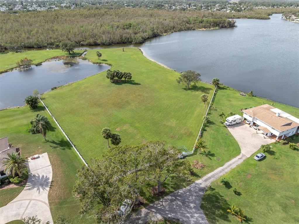 An aerial view shows a large grassy lot bordered by a lake and trees — 0 SILHOUETTE LANE, HOLIDAY, FL