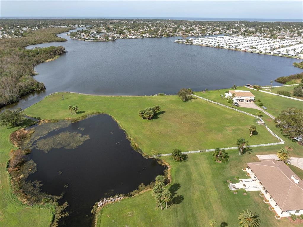 An aerial view shows a large grassy lot with a pond, adjacent to a larger lake — 0 SILHOUETTE LANE, HOLIDAY, FL
