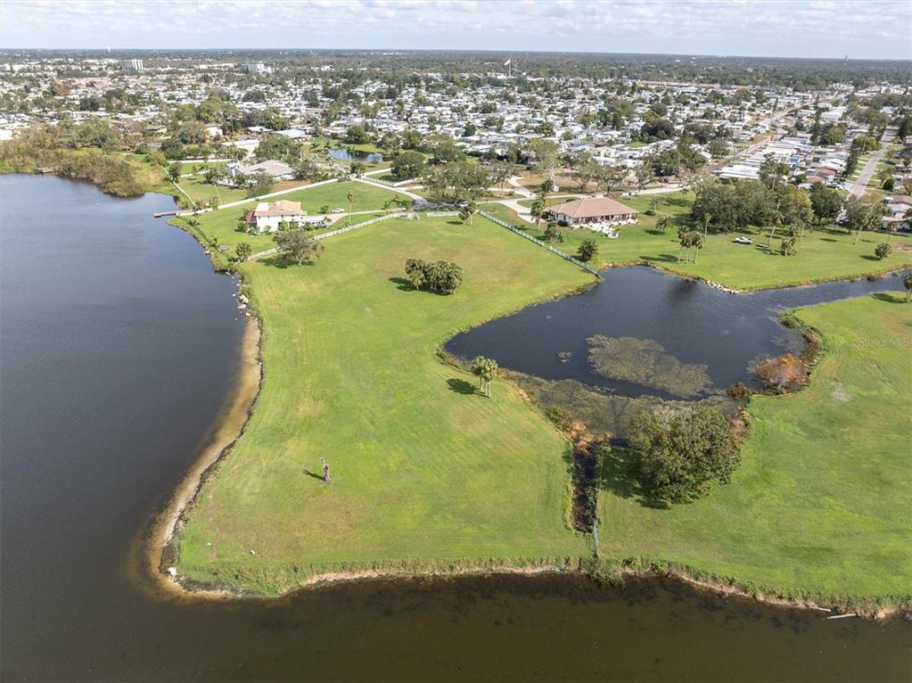 An aerial view shows a large grassy lot bordering a lake and a small pond — 0 SILHOUETTE LANE, HOLIDAY, FL