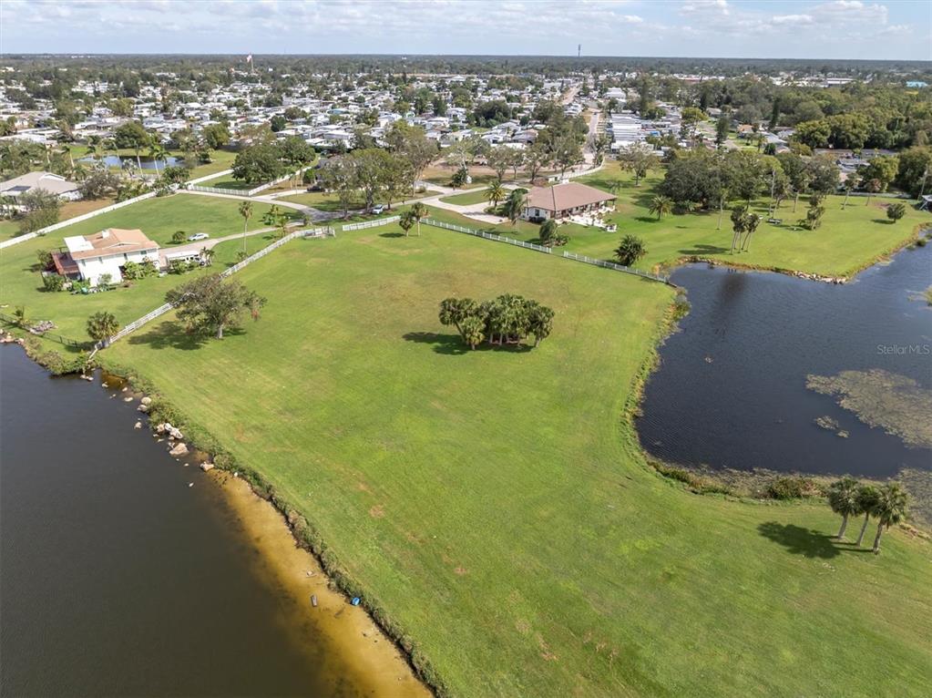 An aerial view shows a large, grassy waterfront lot with a small cluster of trees — 0 SILHOUETTE LANE, HOLIDAY, FL