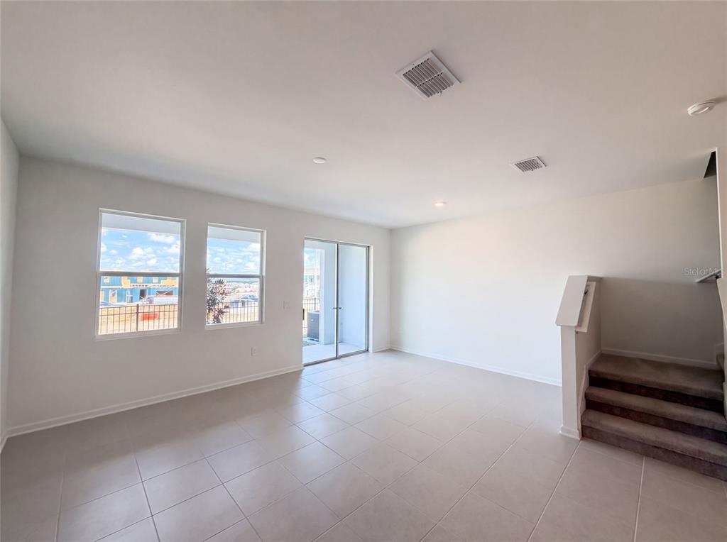 An empty room features light-colored tile flooring, white walls, large windows, a sliding door, and stairs — 3110 KURTZ TERRACE, DAVENPORT, FL