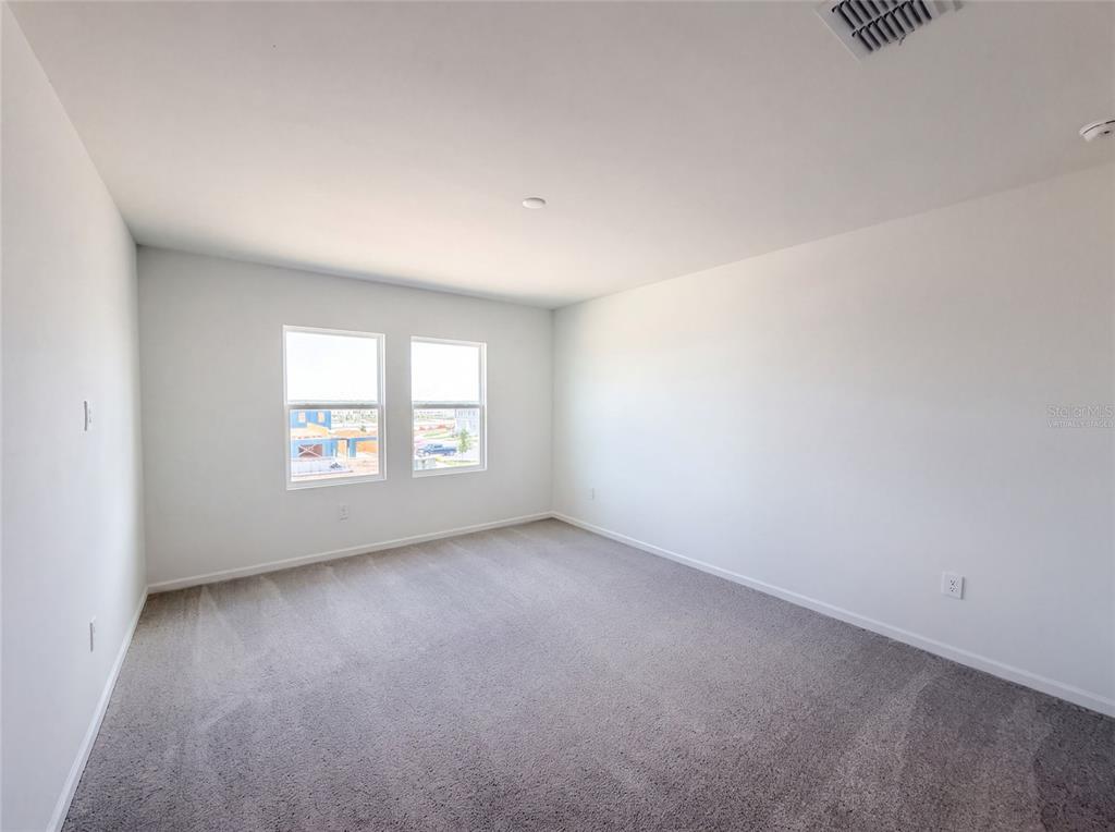 An empty bedroom features gray carpeting, white walls, and two windows overlooking a construction site — 3110 KURTZ TERRACE, DAVENPORT, FL