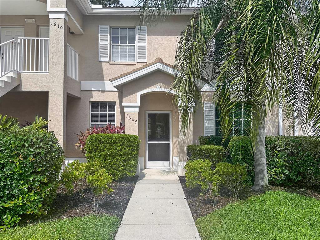 A two-story tan stucco building features a front entrance with a screen door and landscaping — 8065 TIGER COVE UNIT 1604, NAPLES, FL