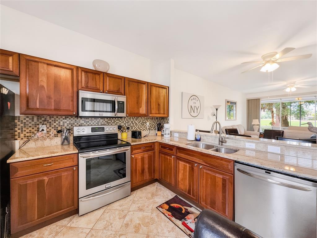 A kitchen features wood cabinets, granite countertops, stainless steel appliances, and a tiled backsplash — 8065 TIGER COVE UNIT 1604, NAPLES, FL