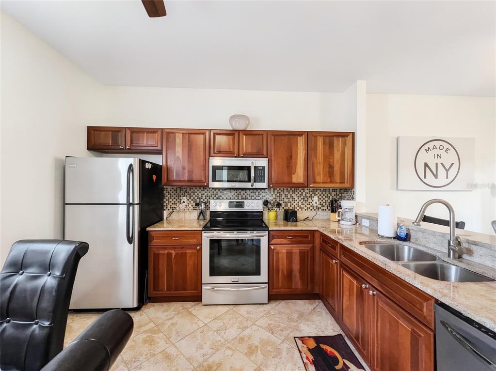 A kitchen features wooden cabinets, stainless steel appliances, granite countertops, and a tiled floor — 8065 TIGER COVE UNIT 1604, NAPLES, FL