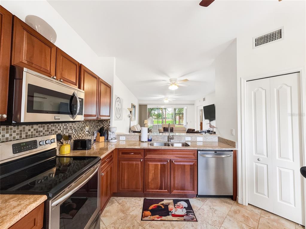 A kitchen with wood cabinets, stainless steel appliances, and tile floors opens to a living area — 8065 TIGER COVE UNIT 1604, NAPLES, FL